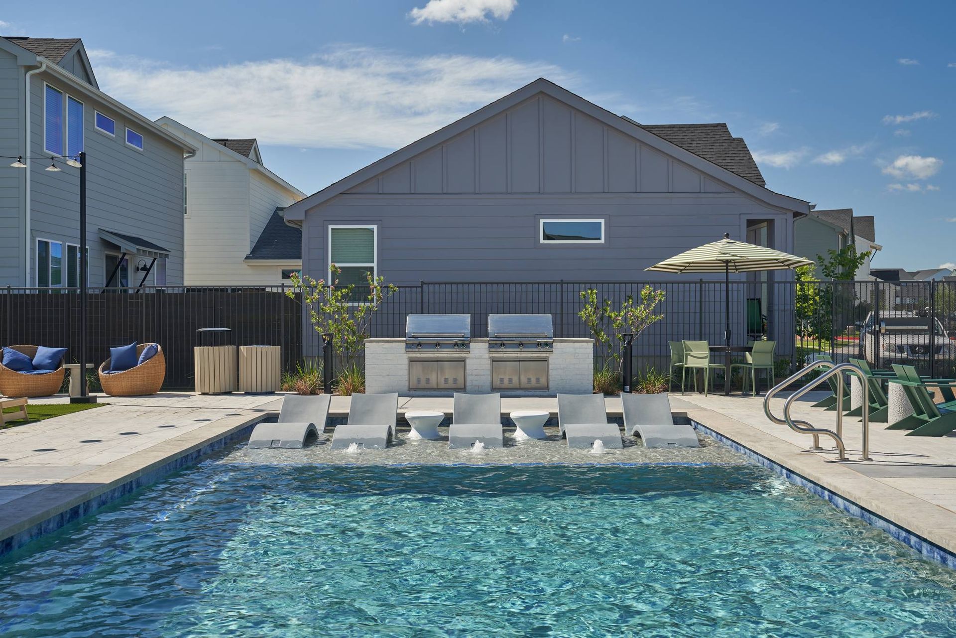 Swimming pool with lounge chairs, grilling area, and modern grey building in the background.