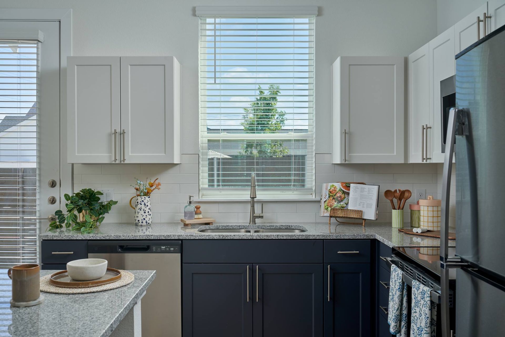 Modern kitchen with white and dark blue cabinets, granite countertops, and a stainless steel refrigerator.