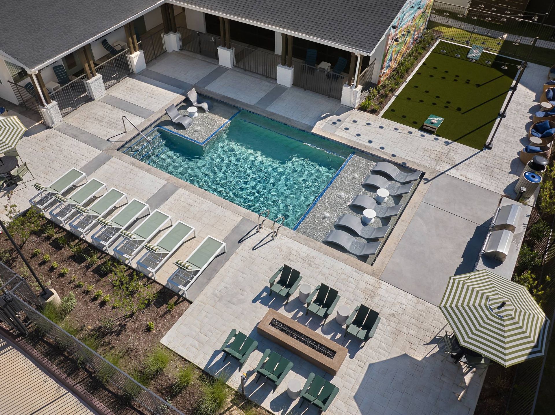 Aerial view of a rectangular pool with lounge chairs and fire pit. Patio furniture surrounds the pool in an outdoor setting.