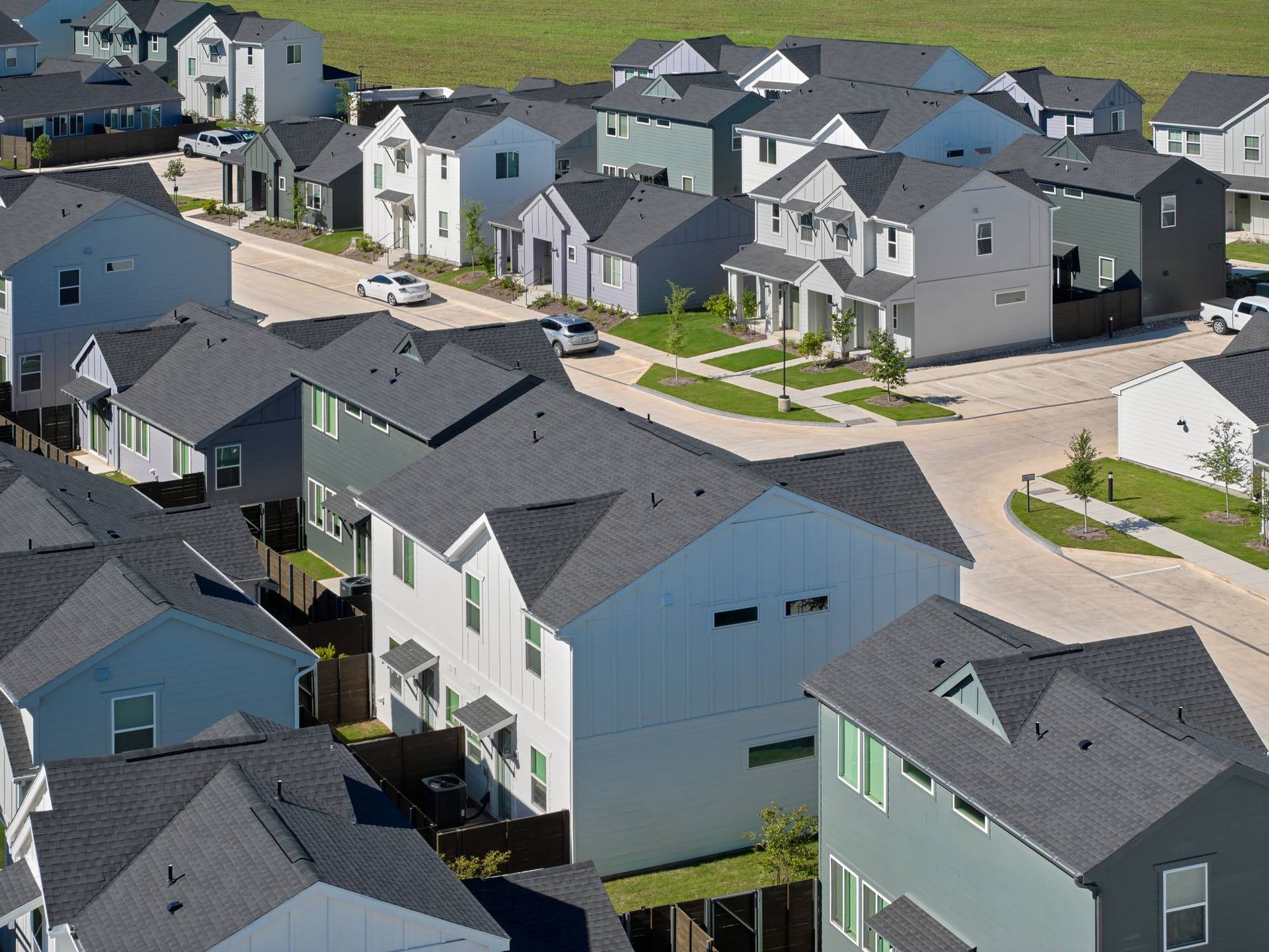 Aerial view of a suburban neighborhood with rows of houses in various shades of gray, blue, and green.