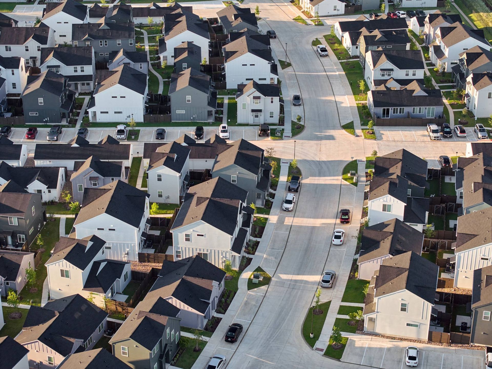 Aerial view of a suburban neighborhood with rows of modern houses and a central road.