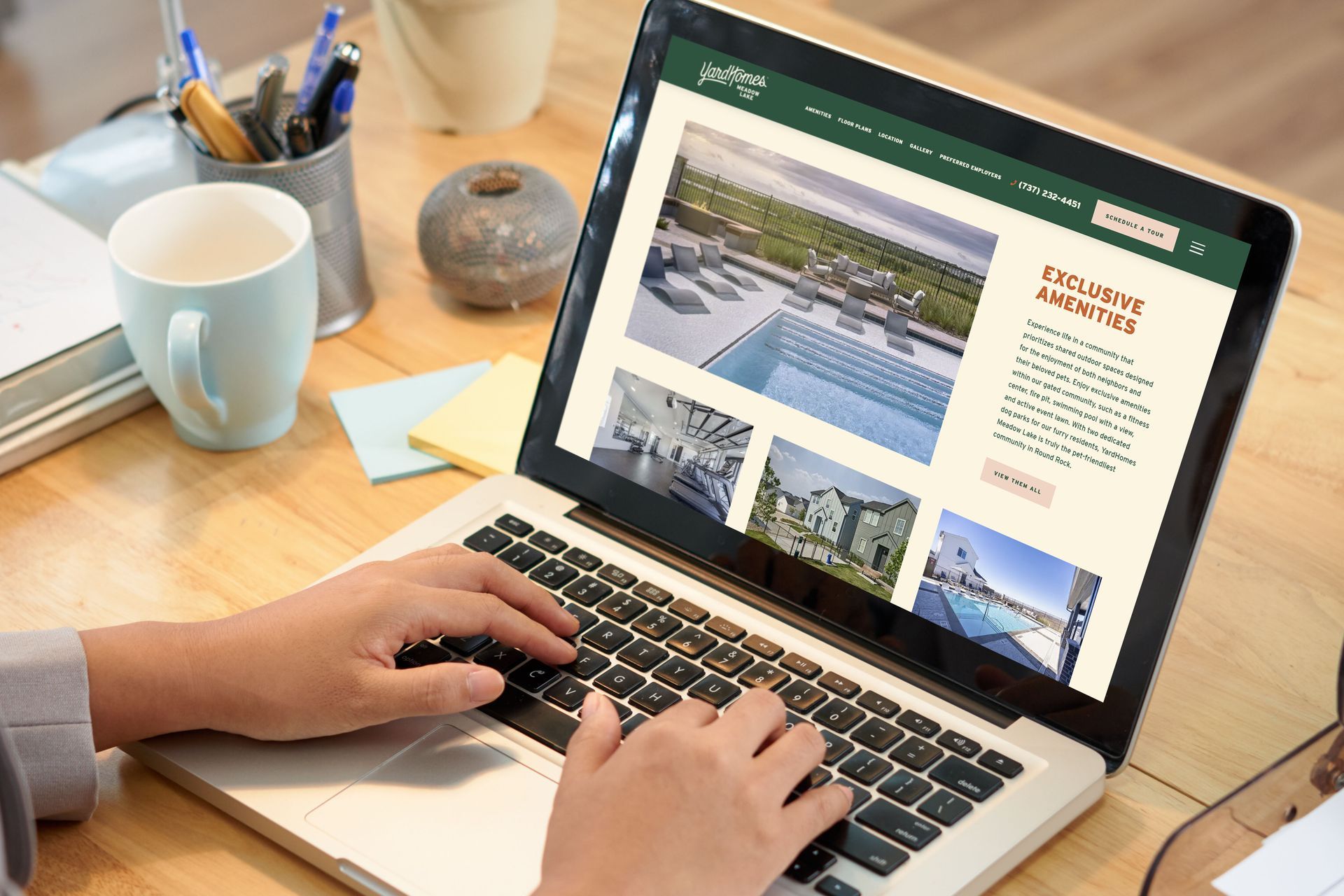 Person using a laptop, browsing a website with pool images on a wooden desk.