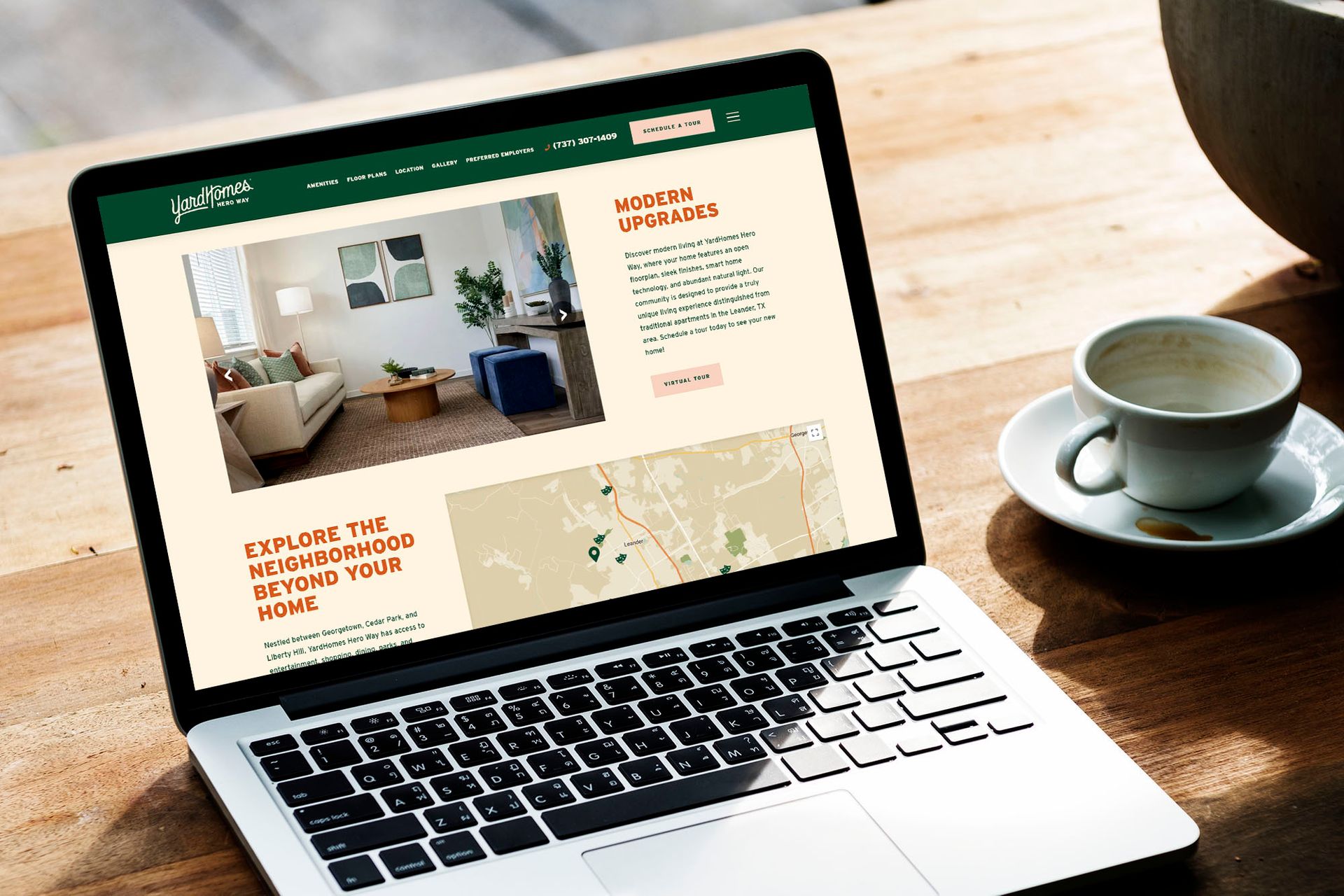 Laptop displaying a website on a wooden table next to a cup and saucer.