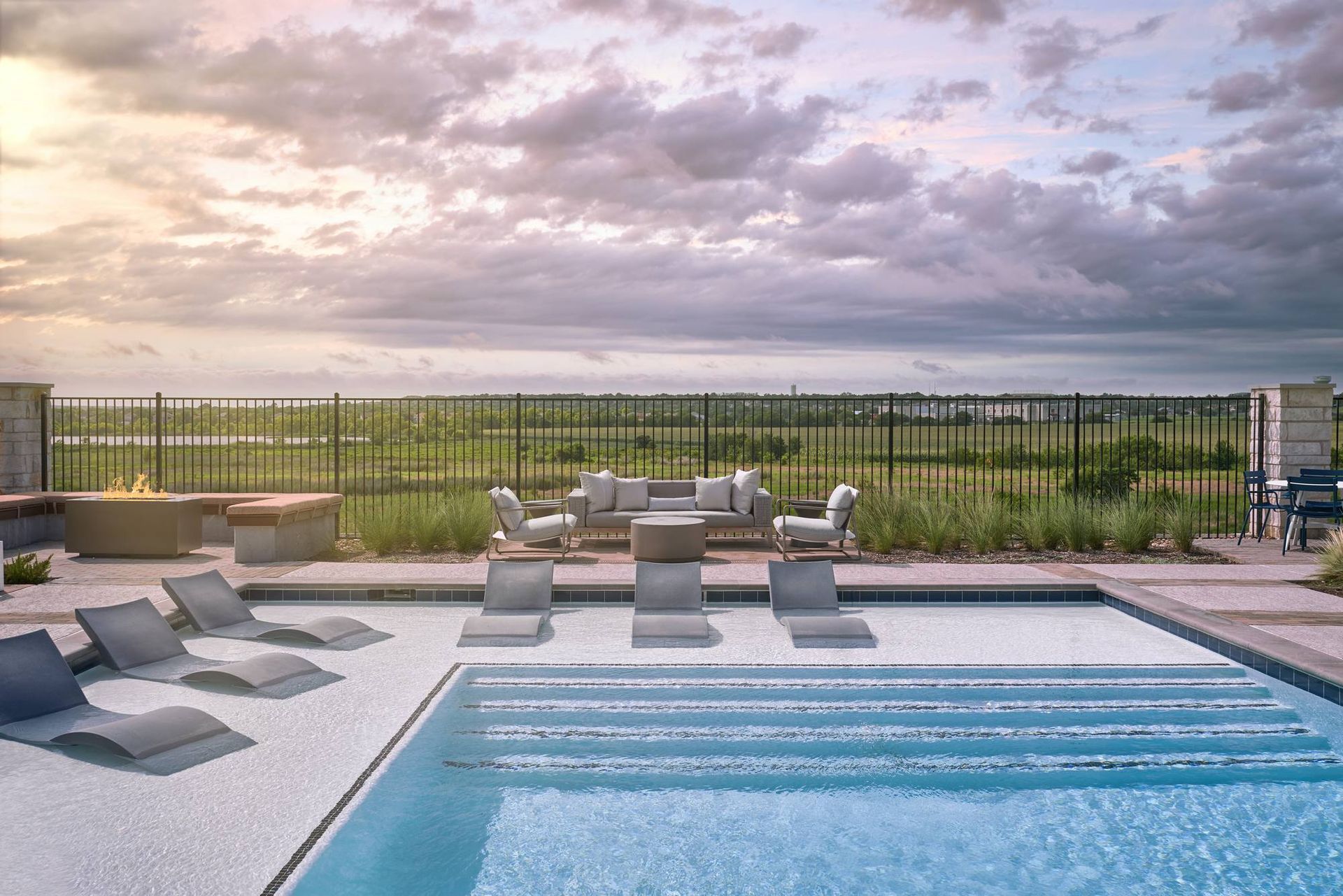 Swimming pool with lounge chairs, outdoor seating, and fire pit under a cloudy sky.