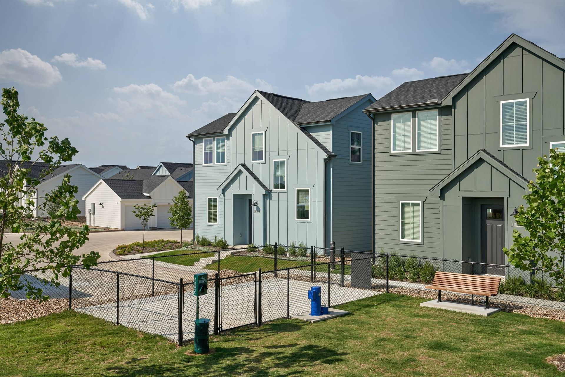 Row of modern townhouses with a small dog park in the foreground, under a blue sky.
