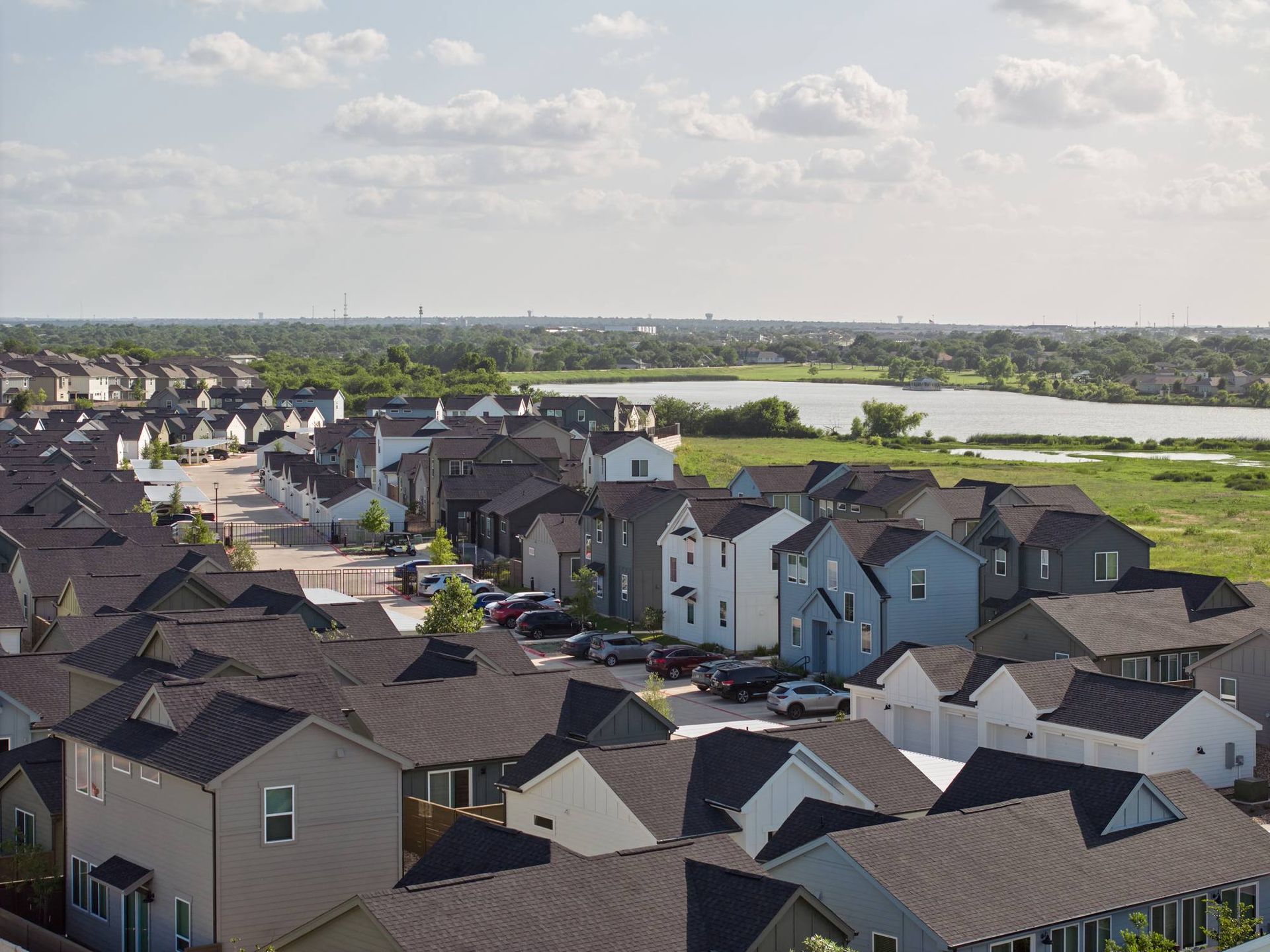 Residential neighborhood with rows of houses, a lake, and a cloudy sky.