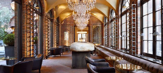 A long hallway with tables and chairs and a chandelier hanging from the ceiling.