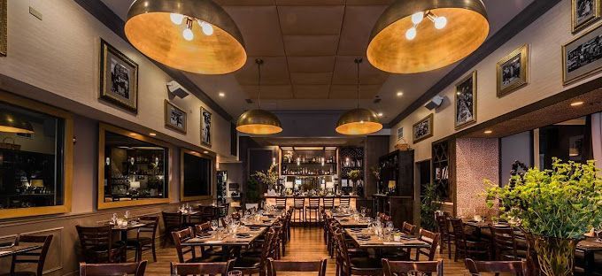 A restaurant with a lot of tables and chairs and a lot of lights hanging from the ceiling.