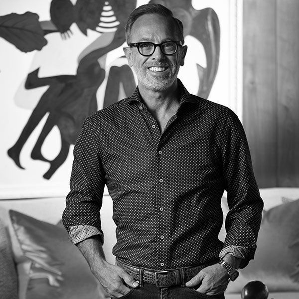 A man wearing glasses and a polka dot shirt is standing in front of a painting.