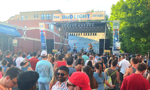 A crowd of people are standing in front of a stage at a bud light stage.