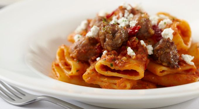 A white plate topped with pasta and meat with a fork.