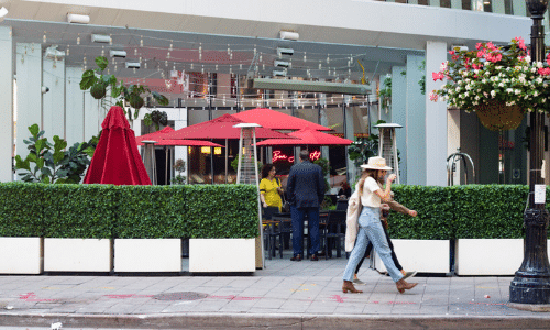 A group of people are walking down a sidewalk in front of a restaurant.