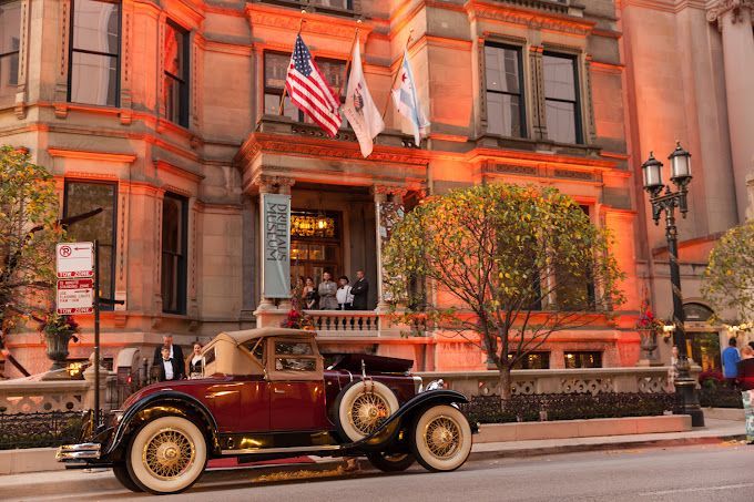 An old car is parked in front of a large building.