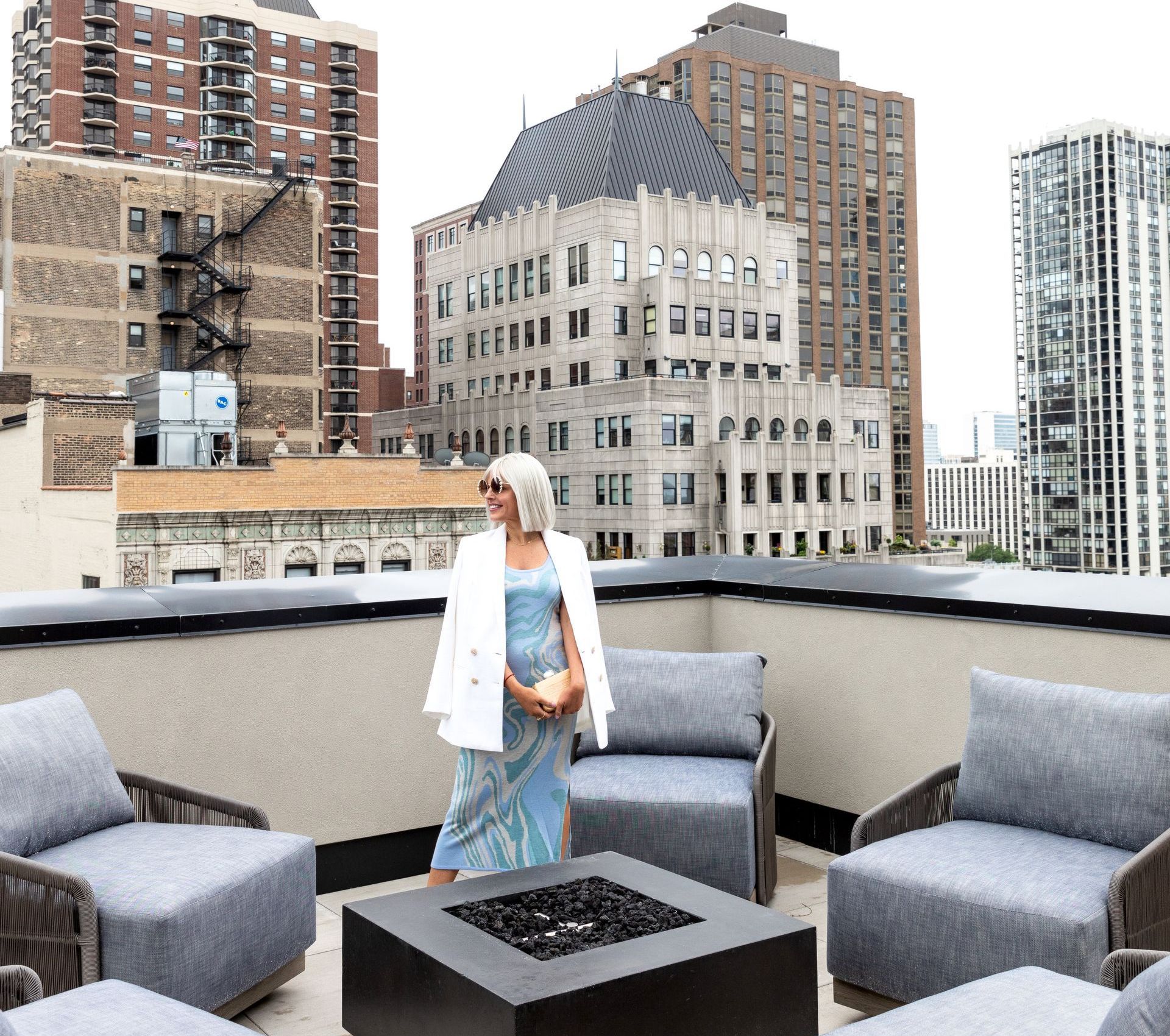 A woman is standing in front of a fire pit on a rooftop.