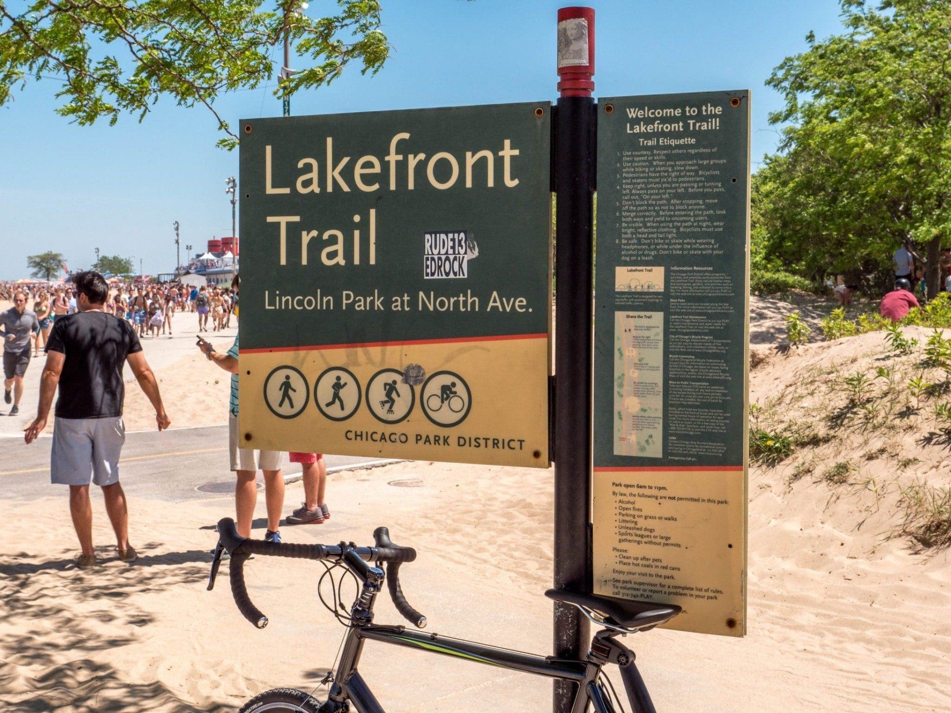 A bicycle is parked in front of a lakefront trail sign