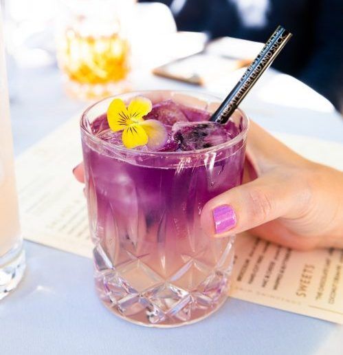 A person holding a purple drink with a yellow flower on top.