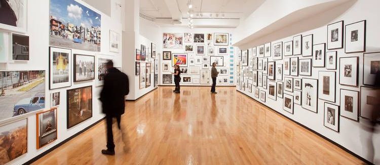 A group of people are standing in a museum looking at pictures on the walls.