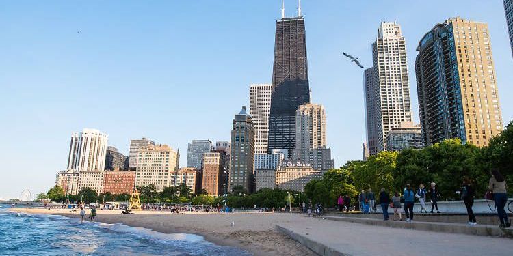 A group of people are walking along a beach in front of a city skyline.