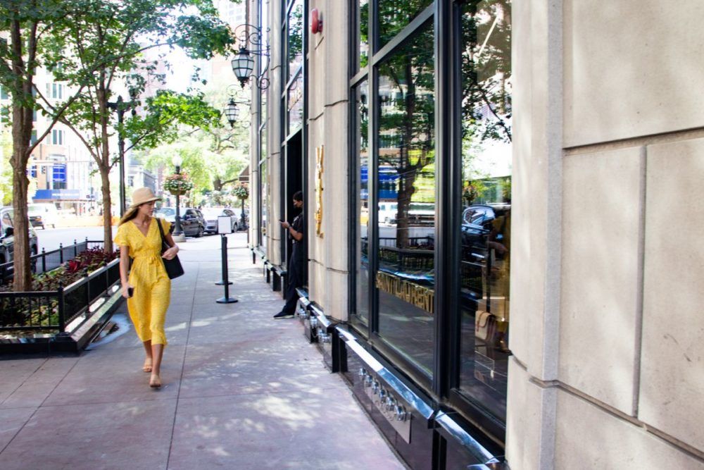 A woman in a yellow dress is walking down a sidewalk in front of a building.