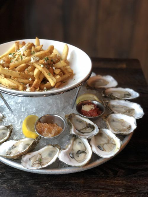 A plate of oysters and french fries on ice on a table.