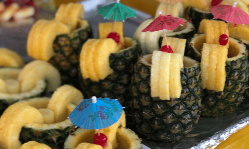 A bunch of pineapples filled with fruit and umbrellas on a table.