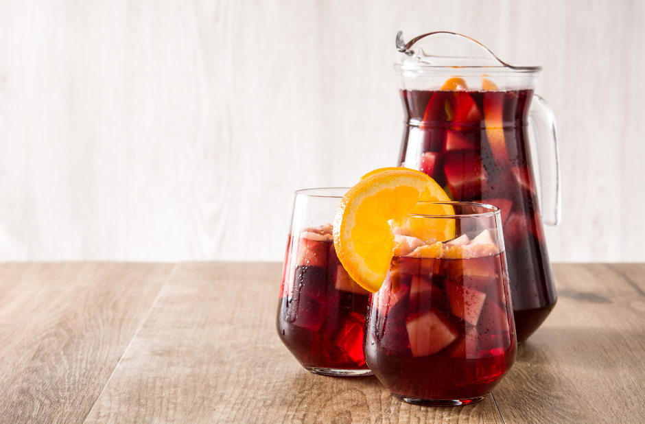 A pitcher and two glasses of sangria on a wooden table.
