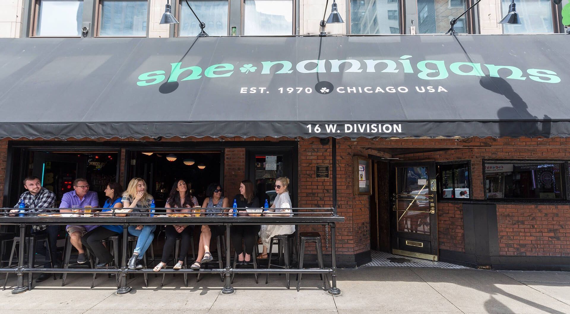 A group of people are sitting at tables outside of a restaurant.