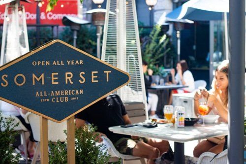 A group of people are sitting at tables in front of a somerset all-american club sign.