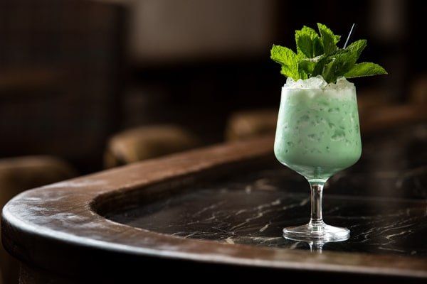 A green cocktail with mint leaves on top is sitting on a bar.