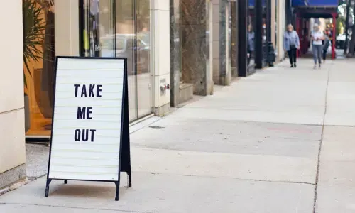 A sign on the sidewalk says `` take me out ''.