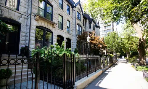 A row of houses with a wrought iron fence along a sidewalk.