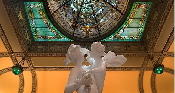 A statue of a woman holding a flower in front of a stained glass window.