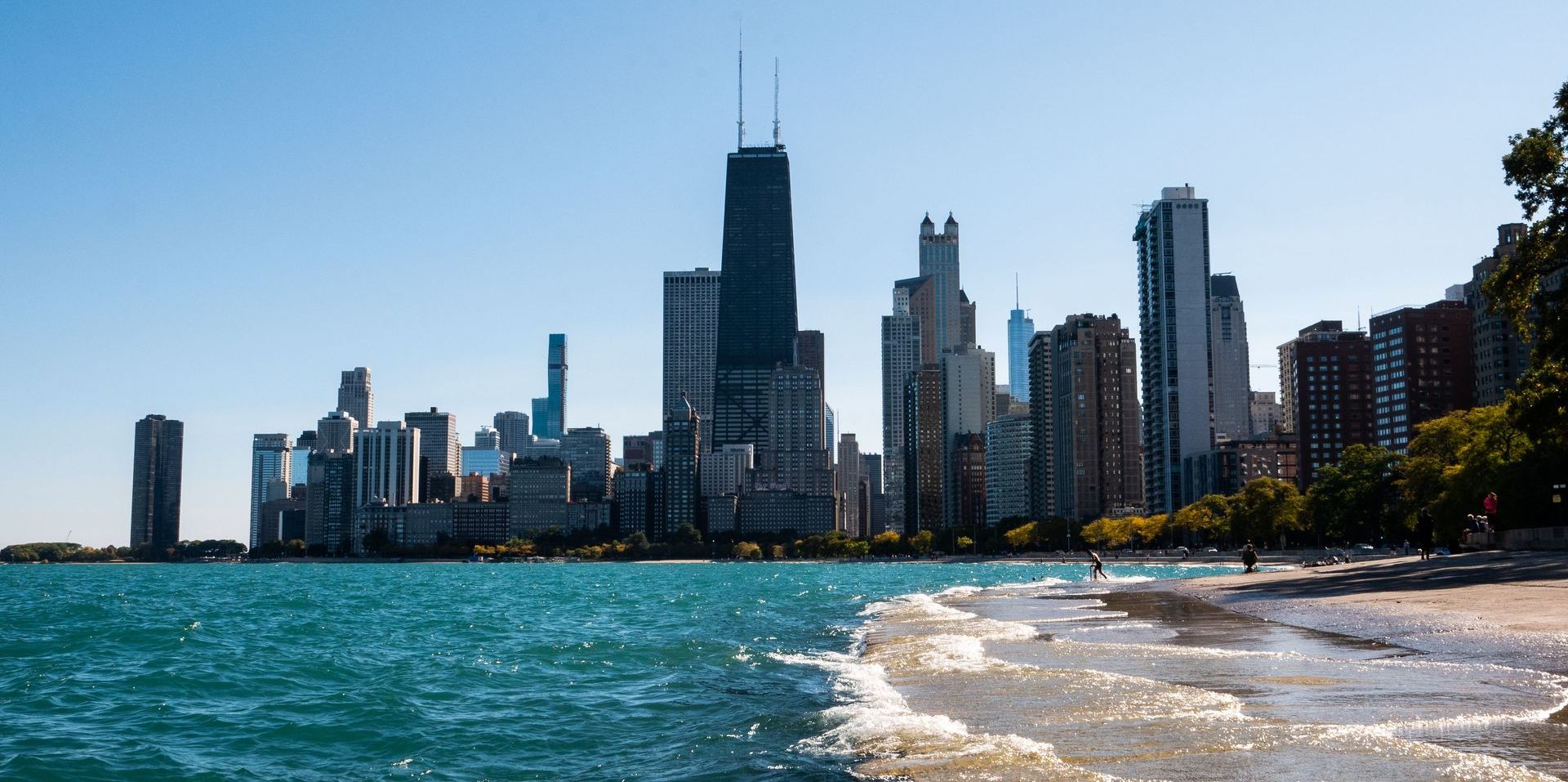 A beach with a city skyline in the background and a body of water in the foreground.
