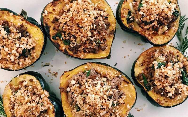 A white plate topped with stuffed acorn squash filled with meat and cheese.