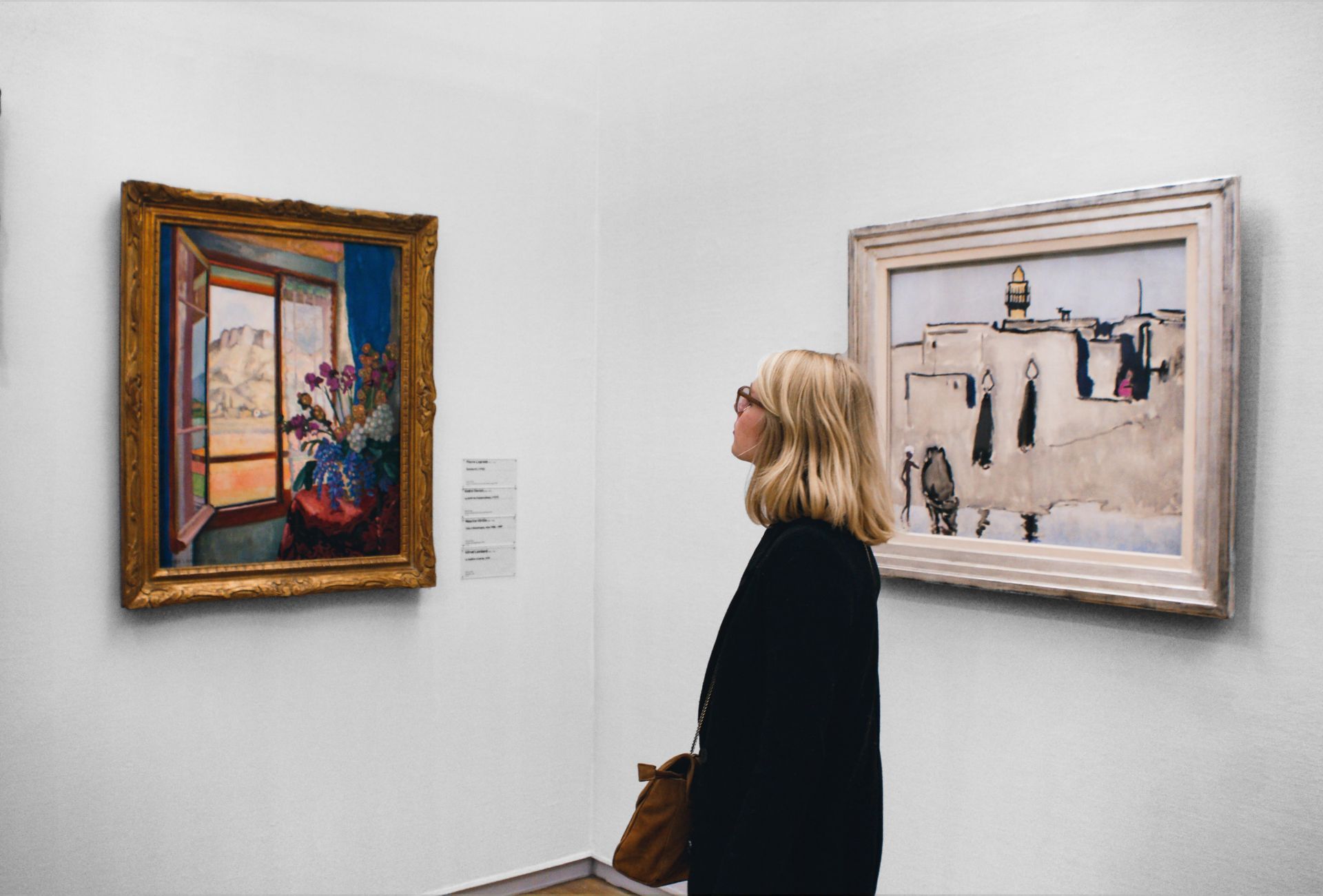 A woman is looking at two paintings in a museum.