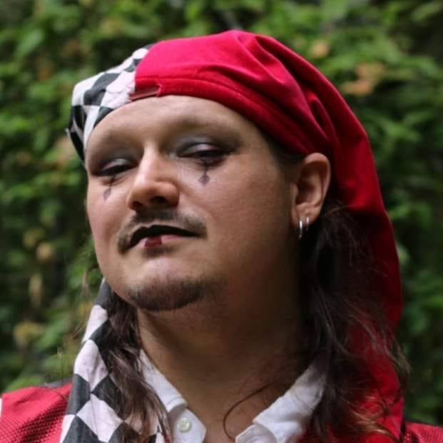 A man wearing a red hat with a checkered scarf around his neck, representing Fortuna.