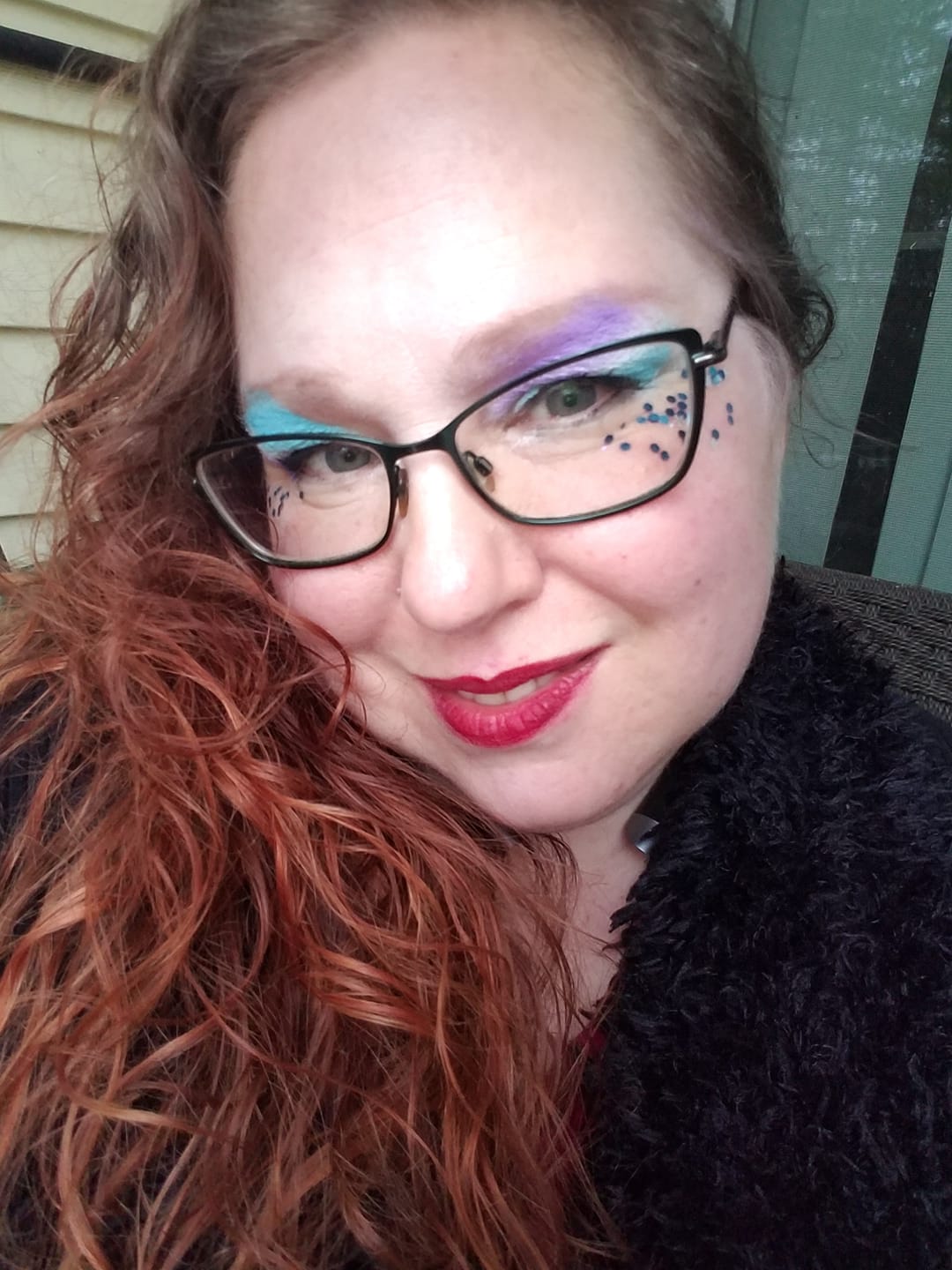 A woman wearing glasses and red lipstick is taking a selfie, representing Aphrodite.