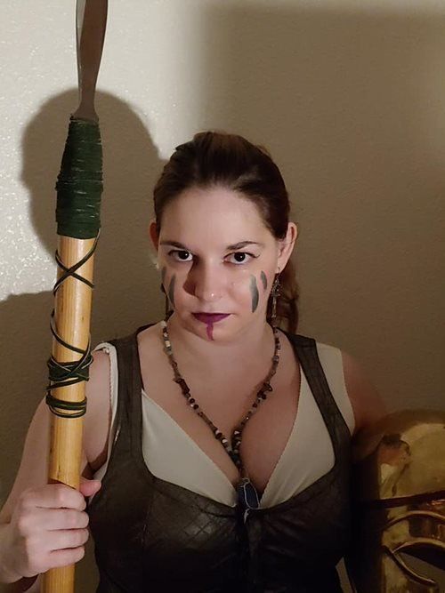 A woman with face paint is holding a wooden stick, representing Athena.