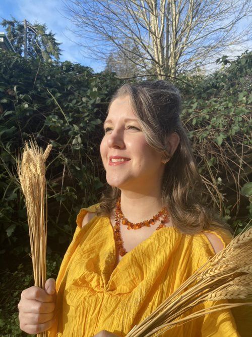 A woman in a yellow dress is holding a bunch of wheat in her hands,  representing Demeter.