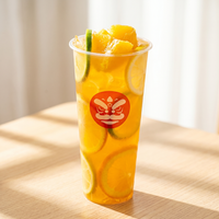 Tall clear cup of orange citrus drink with lemon slices and mango chunks, topped with a lime wedge and red logo