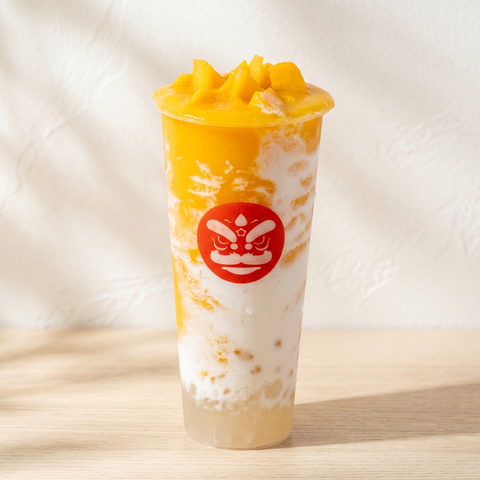 Mango smoothie in a clear cup with a red logo, topped with mango chunks and swirls of cream