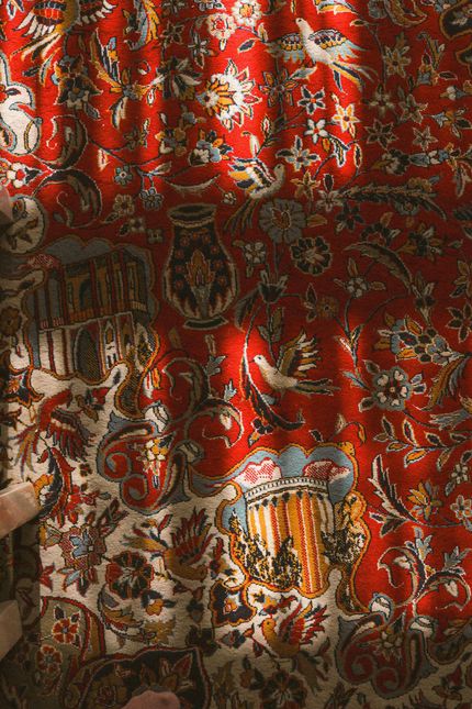 Red patterned curtain with ornate gold, blue, and cream floral designs in sunlight