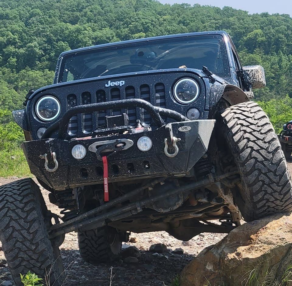 Black Jeep Wrangler crawling over rocks on a rugged off-road trail, front view with oversized tires