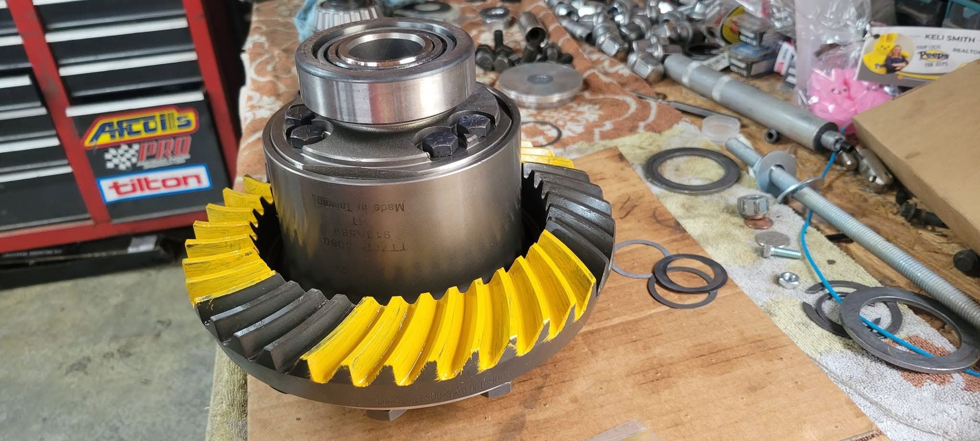 Yellow ring gear on a workbench beside a metal bearing housing and scattered tools.