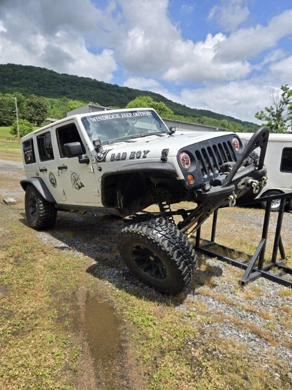 White Jeep Wrangler on a gravel trail with off-road gear, mountains and cloudy sky in the background