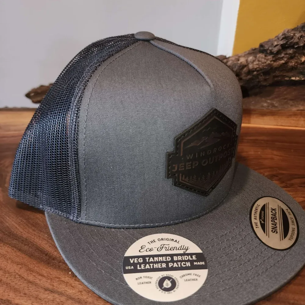 Gray mesh trucker cap with black patch and tan underside on a wooden surface
