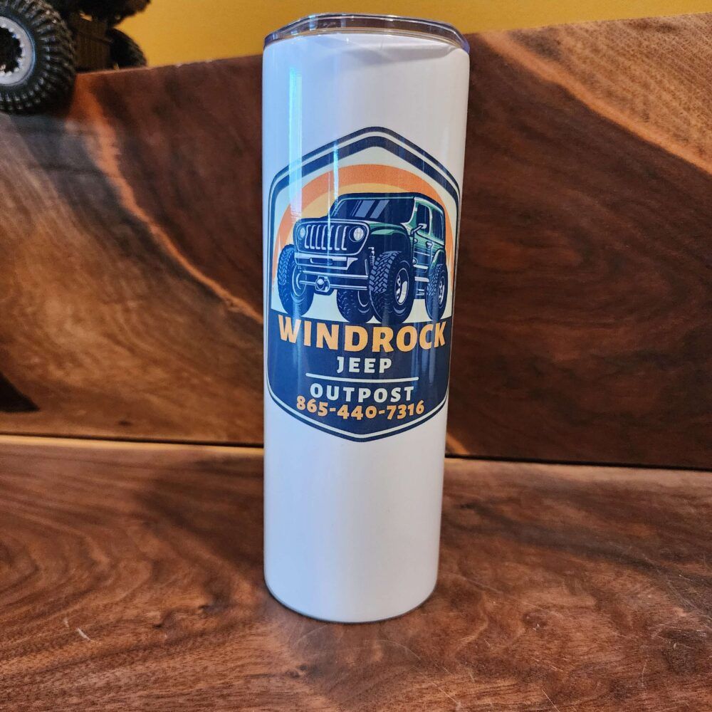 White tumbler with Windrock Jeep Outpost logo and phone number on a wooden surface.
