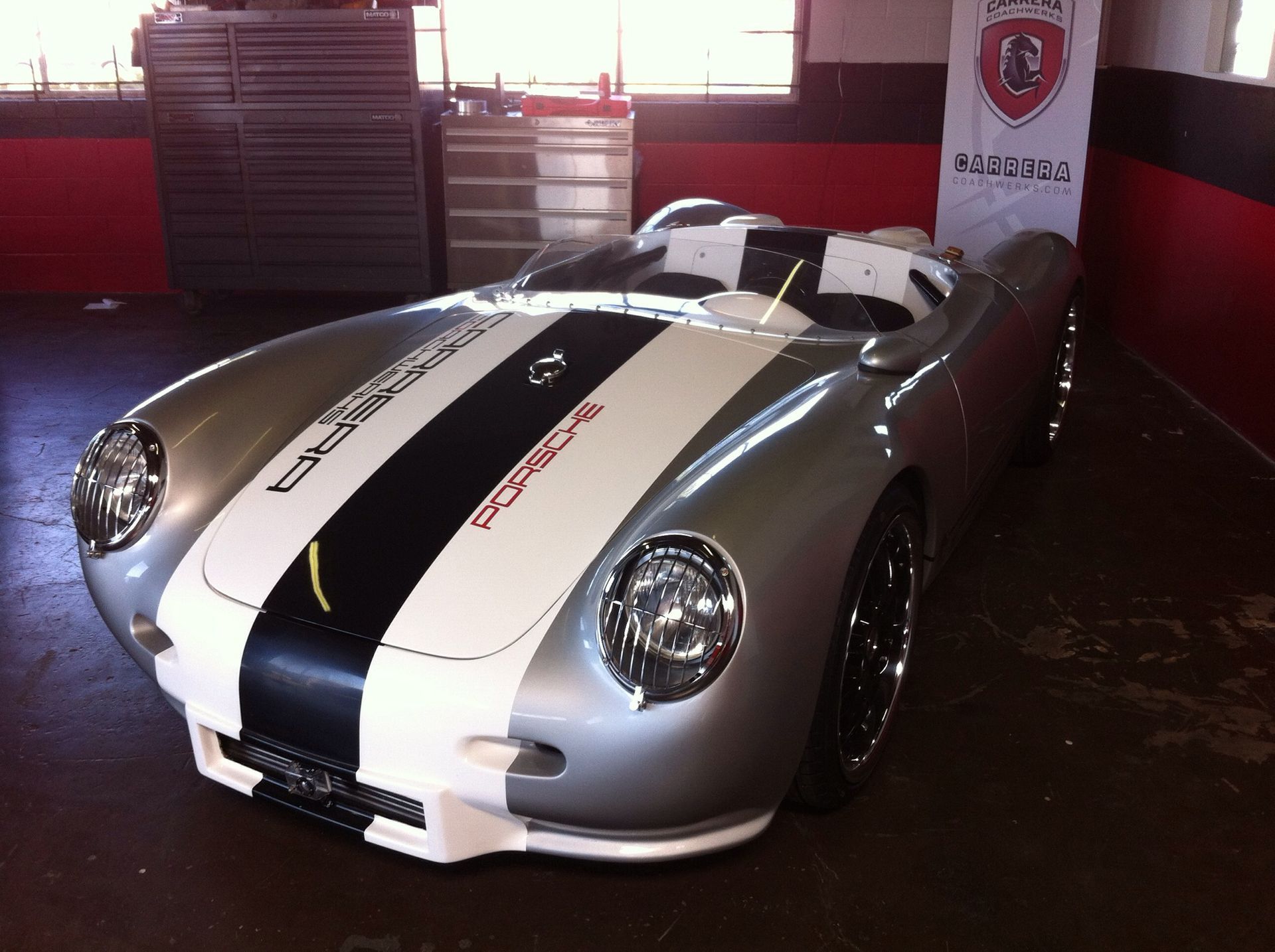 Silver sports car with black and white racing stripes in a garage display area
