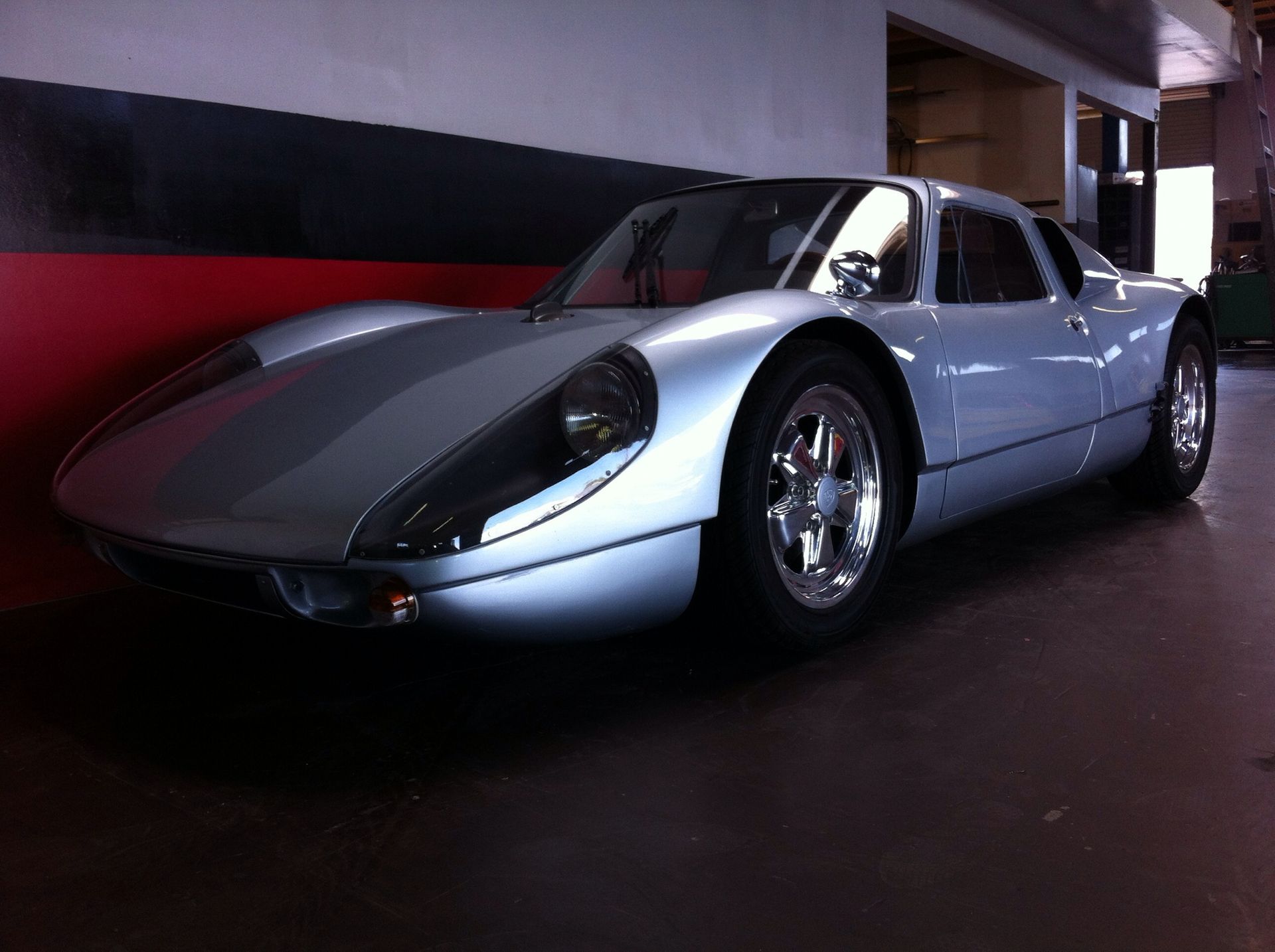 Silver vintage sports car parked indoors in a dim garage, front-left view
