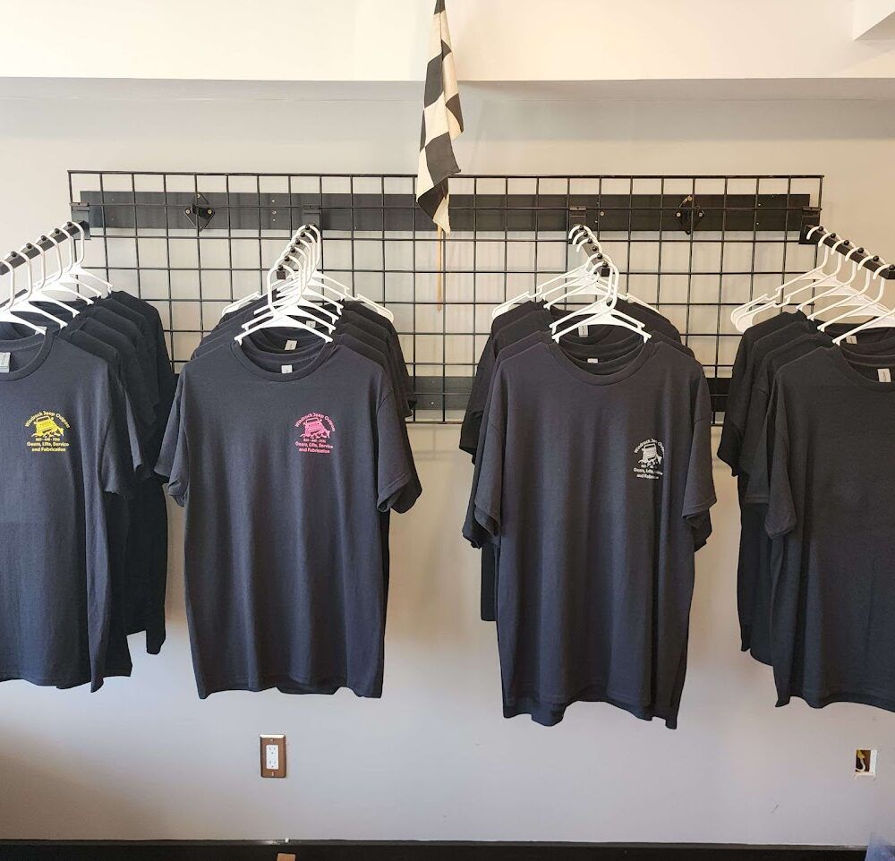 T-shirts hanging on racks in a retail store, mostly dark blue and black with small logos.